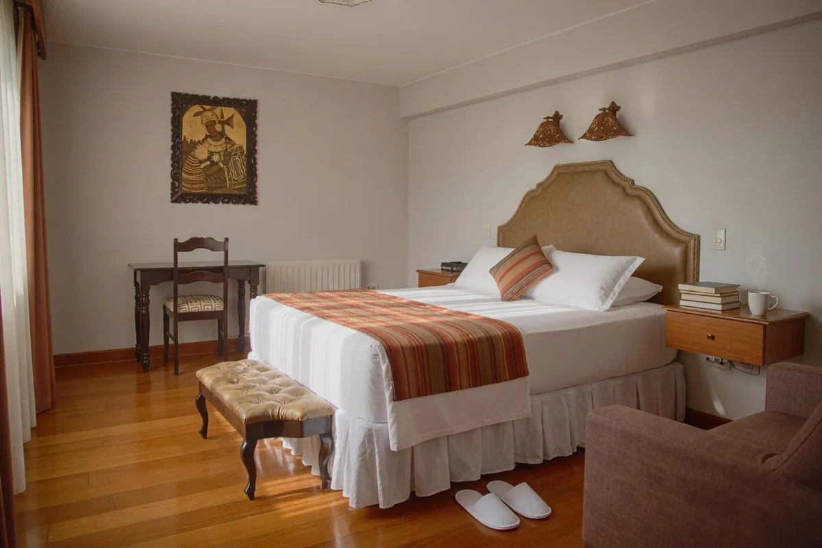 Chambre coloniale lumineuse au Munay Wasi Inn avec lumière du matin, bureau et chaussons pour un séjour prolongé
