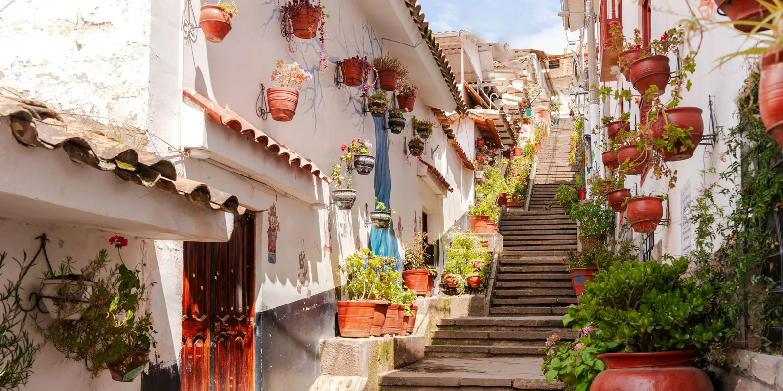 Ruelle de San Blas à Cusco avec murs blancs, pots de fleurs et escaliers en pierre.