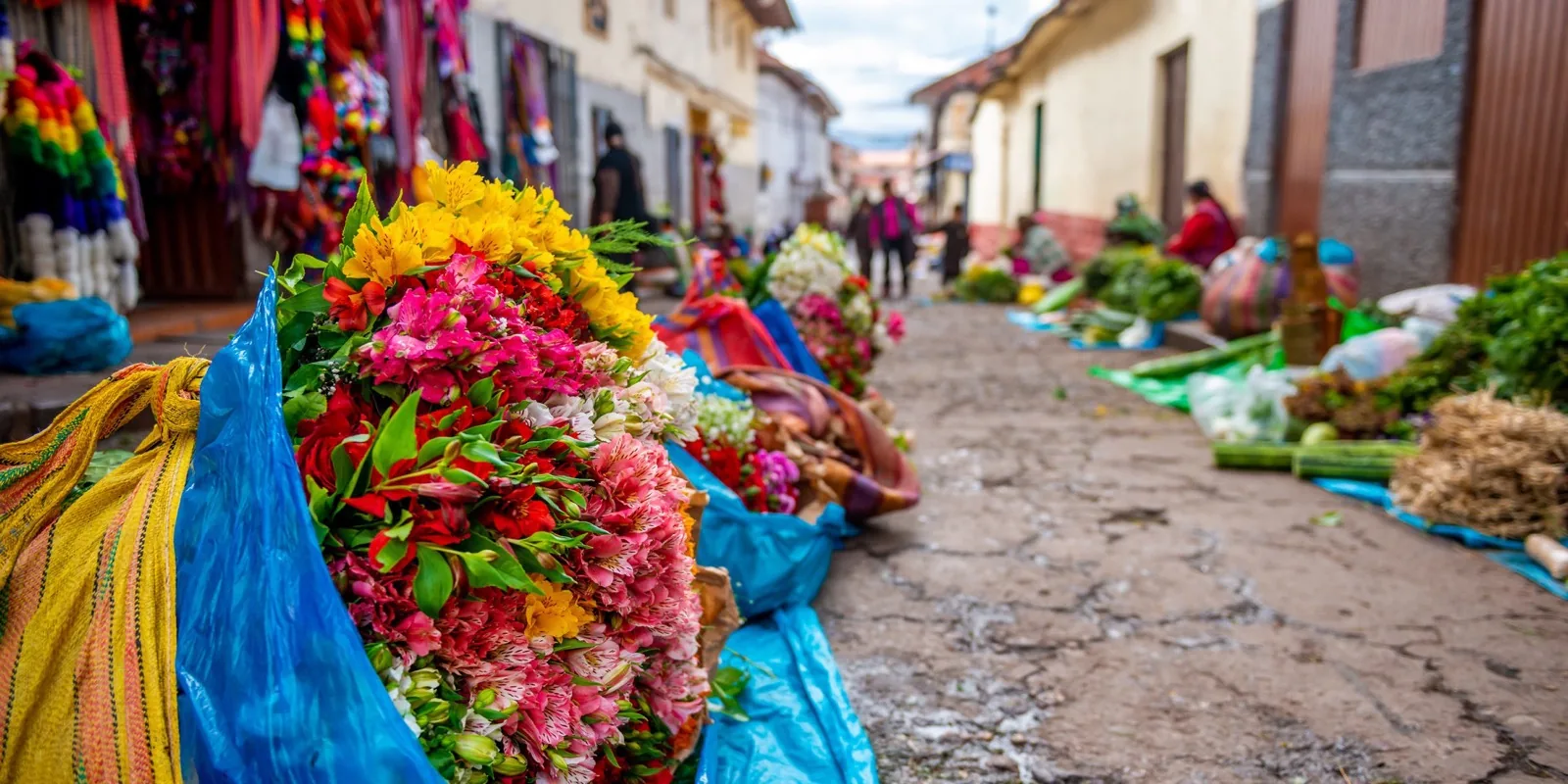 Rue de marché près de San Pedro à Cusco avec bouquets de fleurs, produits et textiles colorés.