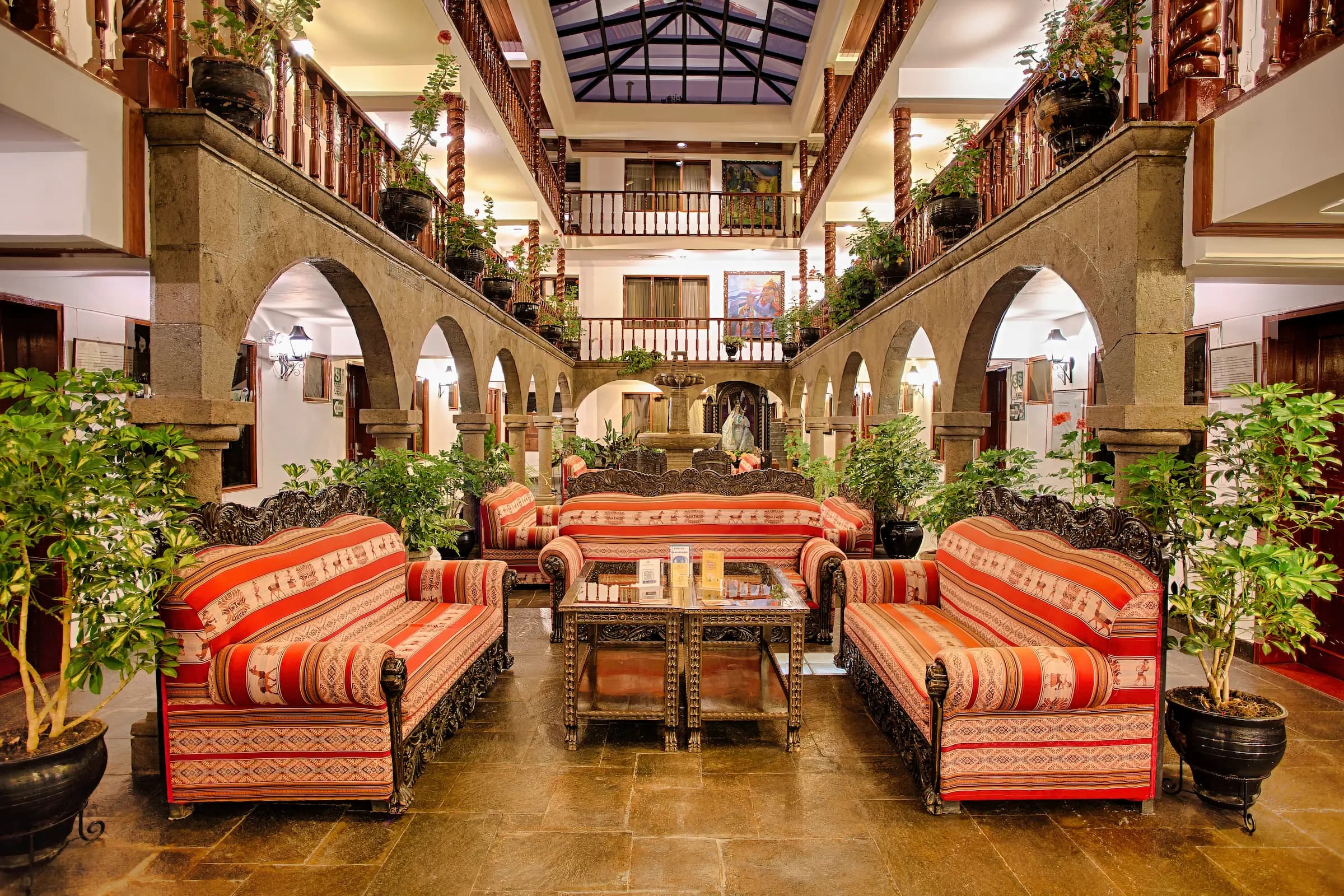 Lobby de estilo colonial del Munay Wasi Inn con muebles de madera ornamentados, tapicería vibrante y abundante vegetación, destacando comodidades modernas en un entorno histórico en Cusco, Perú.